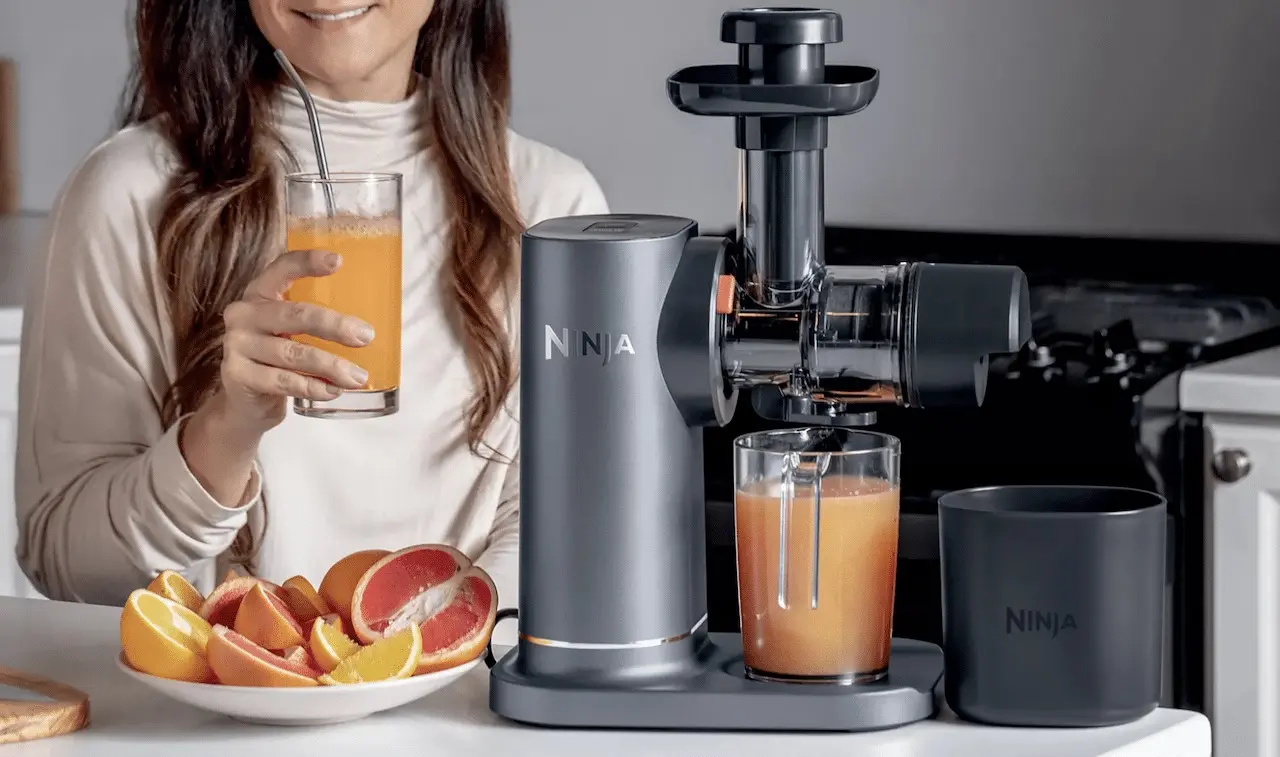 Une femme dégustant un verre de jus de fruits pressé avec l'extracteur de jus Ninja préparant un second verre.