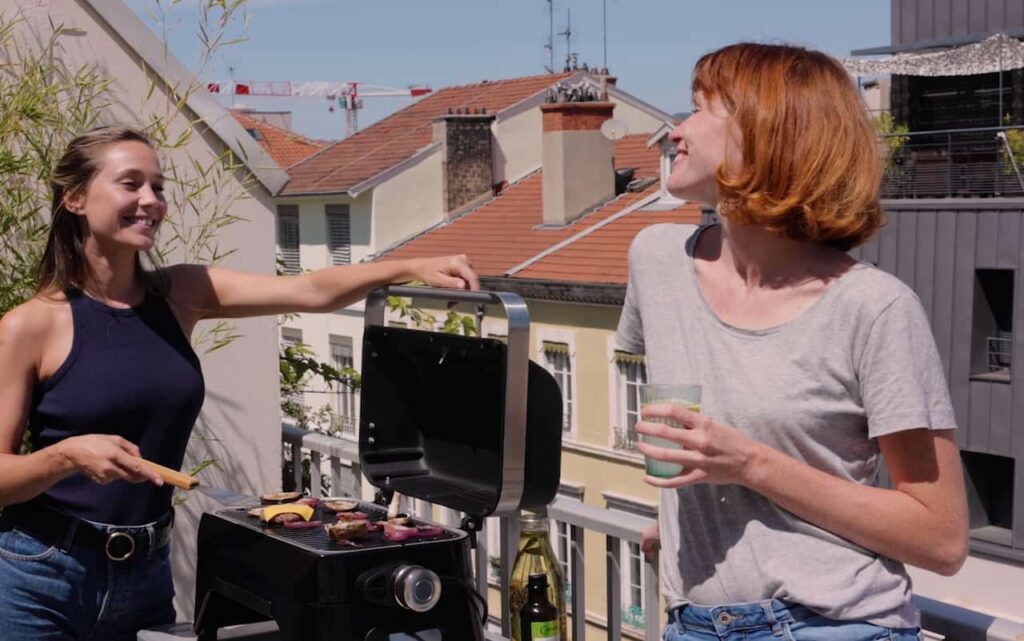 Deux femmes sur une terrasse extérieure, en train de cuire des aliments sur une plancha Campingaz.