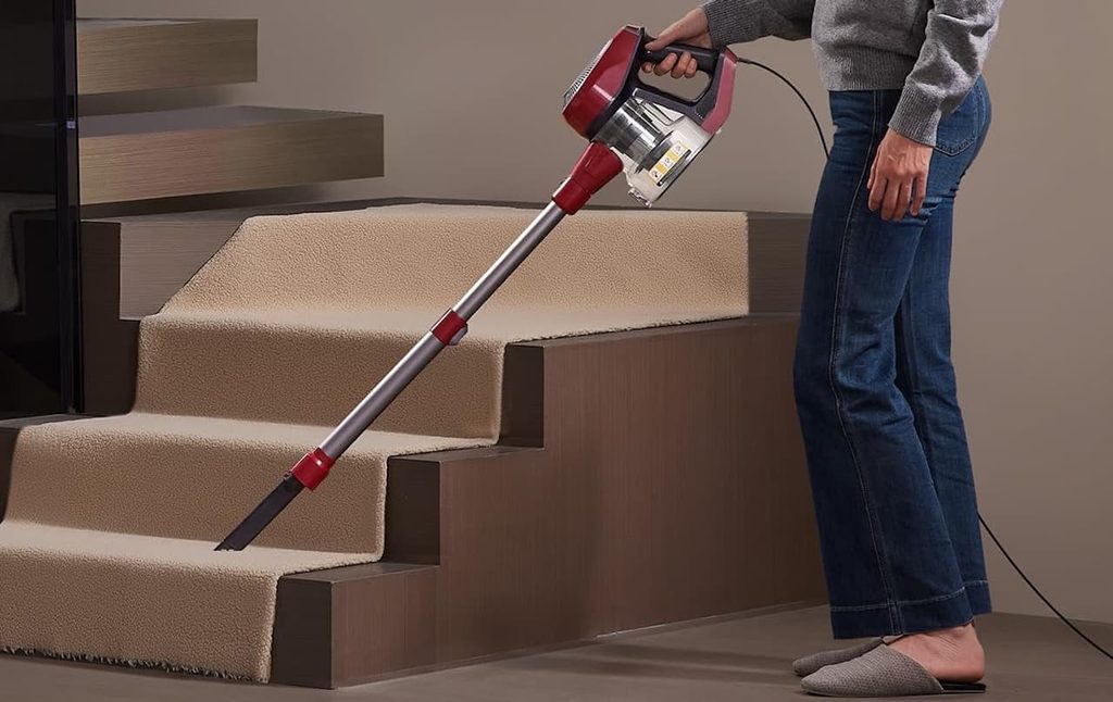 Une femme qui utilise un aspirateur balai avec fil de la marque Vexilar pour nettoyer une moquette sur un escalier.