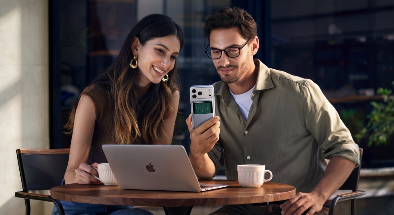 Un homme et une femme prenne un café en travaillant sur leur macbook. L'homme tient un iphone qui se recharge avec le batterie magnétique Ugreen MagFlow Pro 25W 10000 mAh Qi2