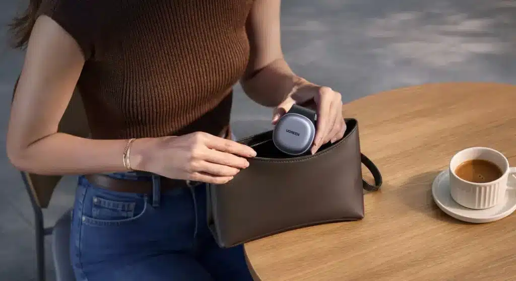 Une femme met dans son sac à main le chargeur Ugreen MagFlow 25W 2 en 1 pliable