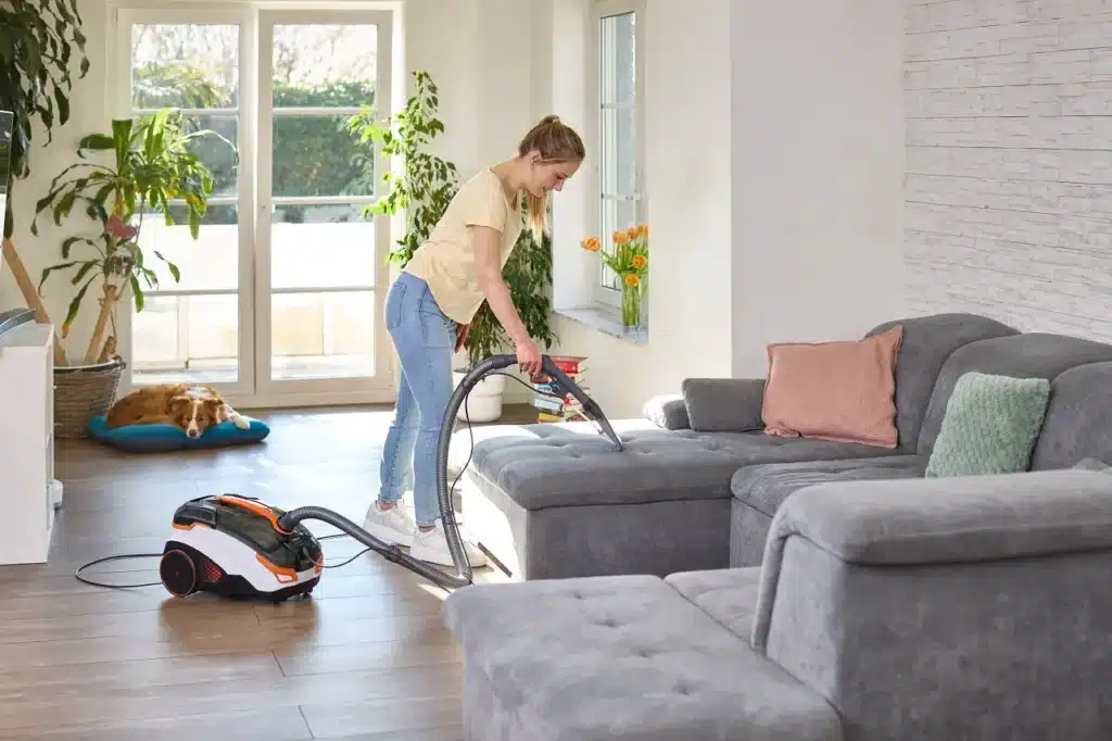 Une femme avec son chien utilise l'aspirateur Amfibia Pro Animal ed la marque THOMAS sur son canapé.